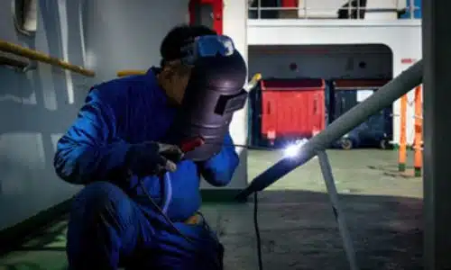 immagine di un addetto alle manutenzioni che ripara il ponte di scarico con una visieta protettiva e la tuta da lavoro blu