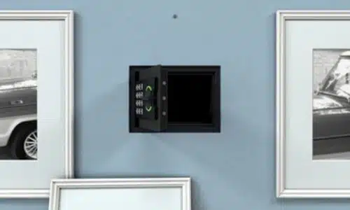 cassaforte resistente al fuoco aperta, di piccole dimensioni, nera e con sistemna di sicurezza a combinazione, su una parete celeste, con due quadri ai lati e uno poggiato sotto che serviva per coprirla
