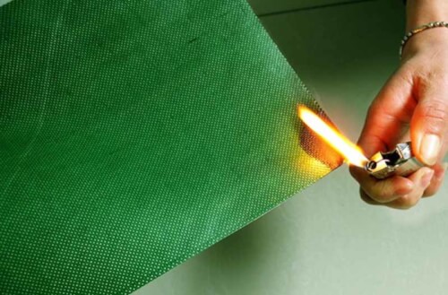 foto di un pannello verde di materiale ignifugo con unàmano che cerca di farlo prendere fuoco con un accendino